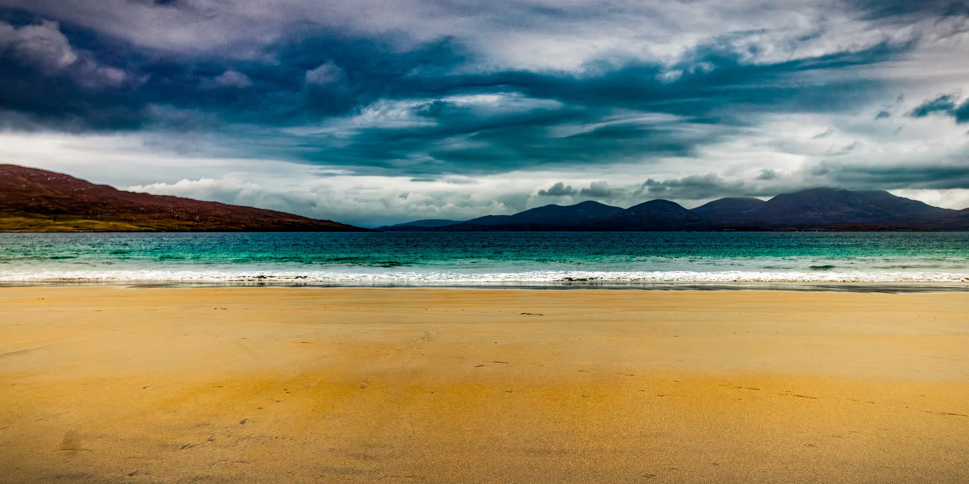 Luskentyre Strand panorama — golden sand, turquoise Atlantic, dark mountains under a storm-lit sky.
