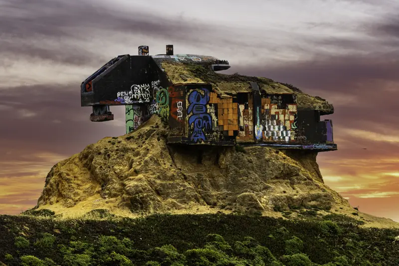 Graffiti-covered wartime coastal bunker on a California bluff, dramatic sunset sky.