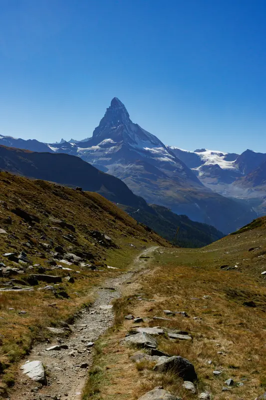 The Matterhorn seen from a high alpine trail above Zermatt, clear blue sky.