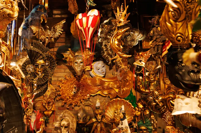 A shop display of elaborate gilded Venetian carnival masks in gold, black, and jewelled colours, densely arranged.