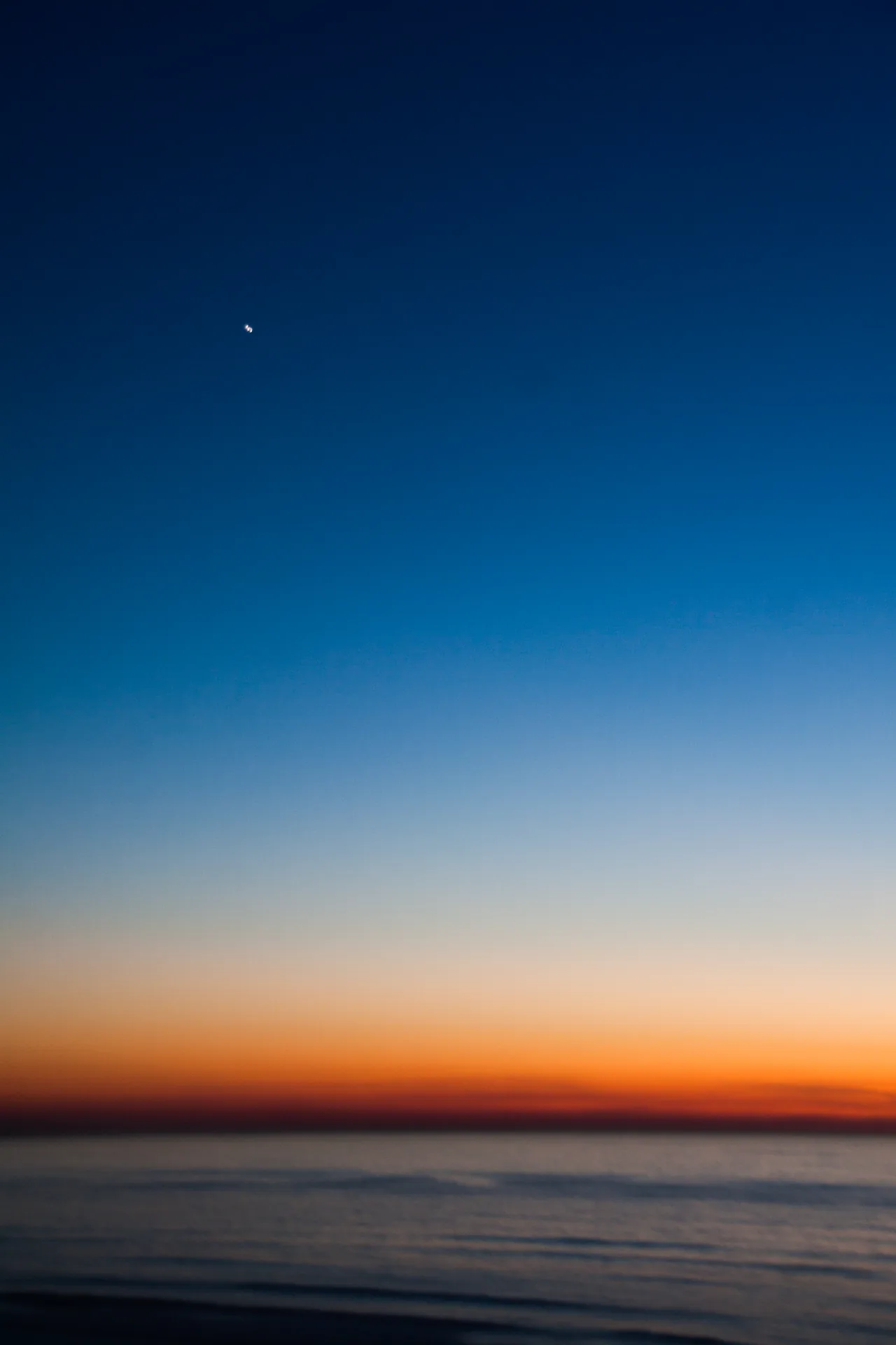 Afterglow — minimalist twilight seascape, deep blue sky gradient to orange on the horizon, sliver of moon.