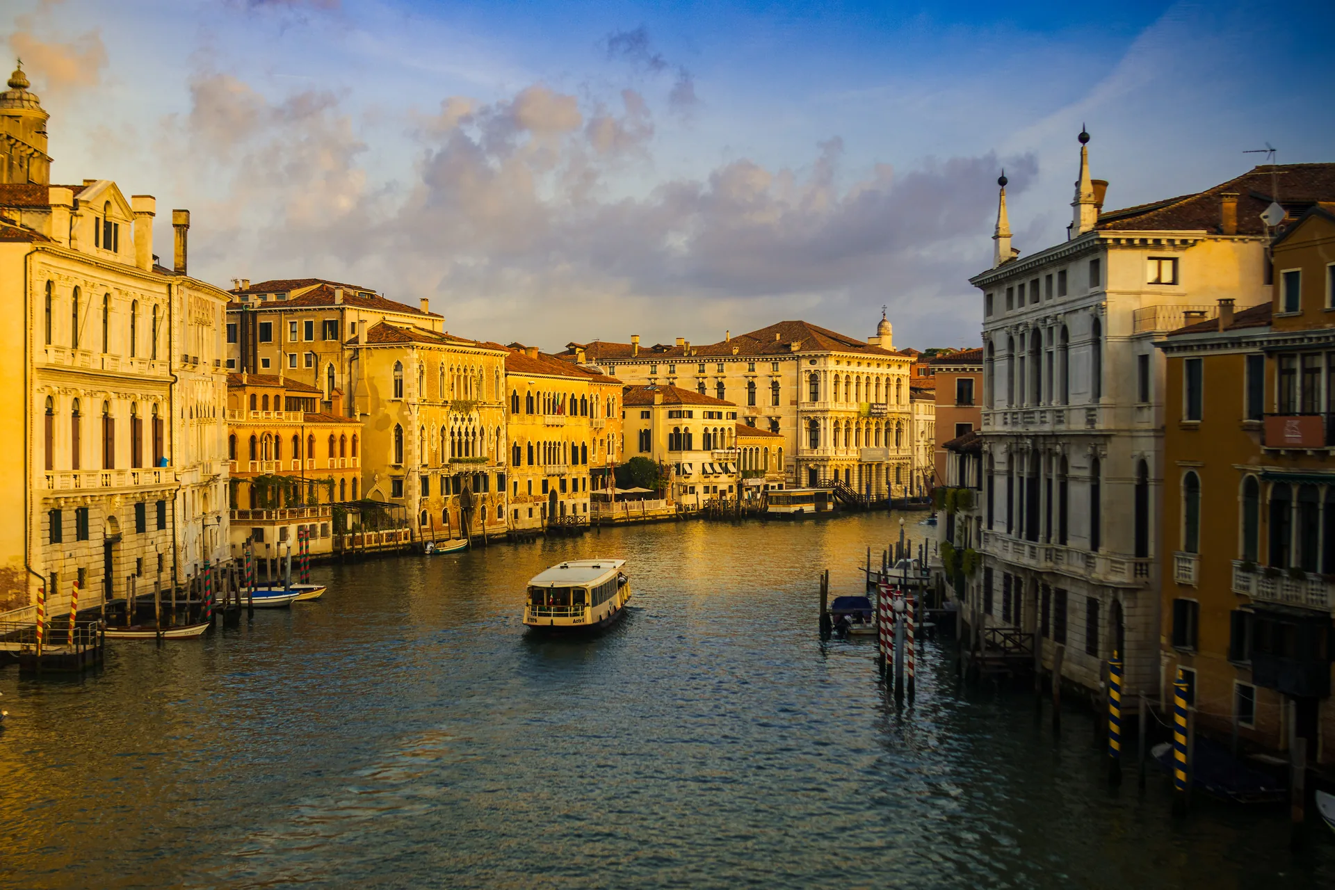 The Grand Canal from the Rialto Bridge area, morning golden light, a vaporetto crossing between Venetian palazzi.